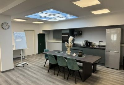 Communal kitchen and dining area with a long dark table, teal chairs, and modern appliances.