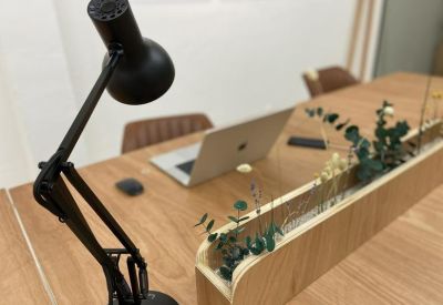 Long wooden coworking desk with a black desk lamp, laptop, and built-in planter box.