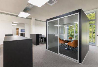 Spacious office interior with a glass-walled meeting pod and orange armchairs.