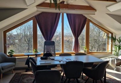 Bright conference room with a large table, grey chairs, and a triangular window overlooking trees.