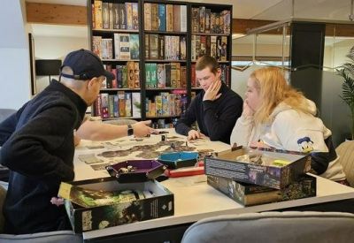 Group of colleagues playing a board game around a large white table in a library-like setting.