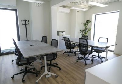 Sunlit office space with several gray workstations and ergonomic mesh chairs.