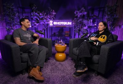 Podcast studio setup with two people in armchairs under purple neon lighting.