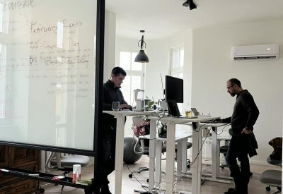 Open-plan office space featuring height-adjustable standing desks and large windows.