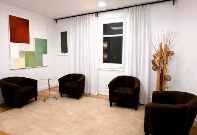 Lounge area with dark brown armchairs, white curtains, and a beige area rug.