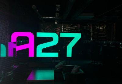 Dark lounge area with glowing neon A27 signage in cyan and magenta.