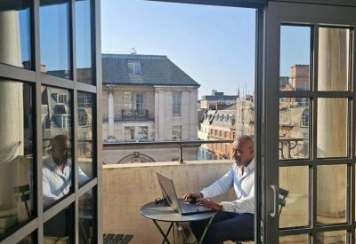 Private balcony workspace with a person on a laptop overlooking city rooftops.