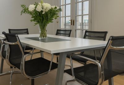 Modern meeting room featuring a white table, mesh chairs, and a large arched glass door.