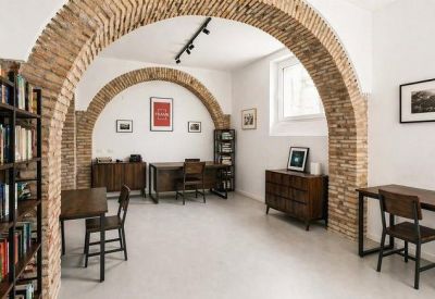 Open workspace with brick arches, wooden desks, and framed art on white walls.