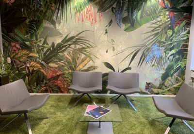 Lounge area featuring four grey armchairs on a green rug set against a tropical jungle mural.