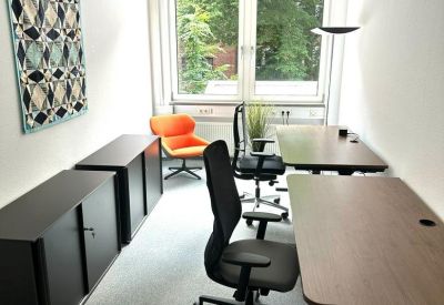 Bright private office featuring two adjustable desks, ergonomic chairs, and a window view.