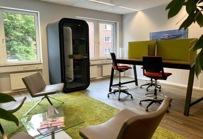 Modern breakout area with a green rug, lounge chairs, and a privacy phone booth.