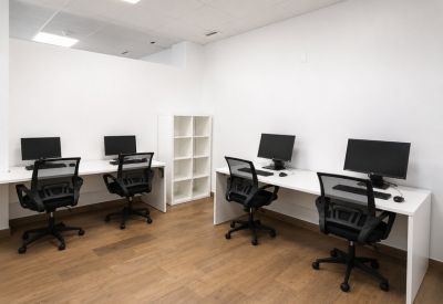 Open-plan coworking area with white desks, ergonomic black chairs, and wooden flooring.