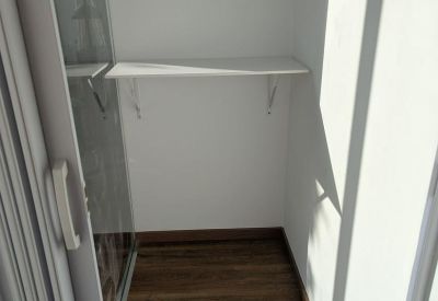 Small white storage nook or closet with a single shelf and wooden flooring.