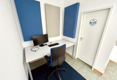 Bright office space with a white desk, blue acoustic wall panels, and a blue office chair.