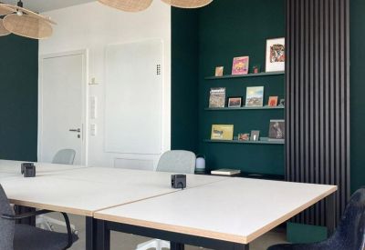 Modern coworking space with large white desks and a deep green feature wall.