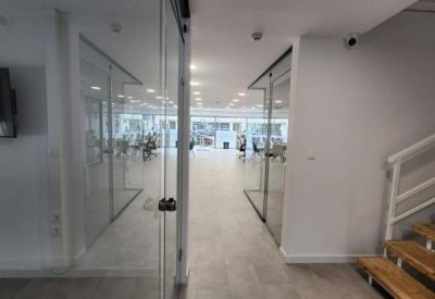 Modern hallway with glass-walled offices and a wooden staircase.