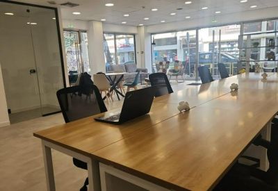 Spacious open-plan workspace with long wooden desks and black ergonomic chairs.