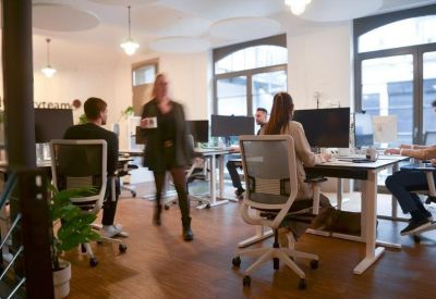 Bright open-plan workspace with white desks, ergonomic chairs, and large windows.