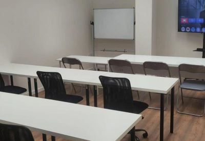 Training or seminar room with rows of white desks, black chairs, and a television screen.
