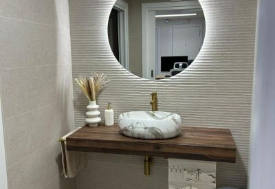 Modern restroom featuring a circular backlit mirror and a stone vessel sink on a wooden vanity.