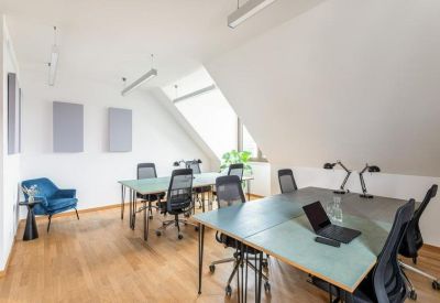Bright attic office with multiple desks, ergonomic chairs, and a blue velvet armchair.