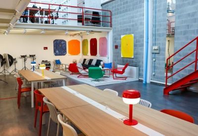 Modern communal area with long wooden tables and vibrant colorful lounge seating.