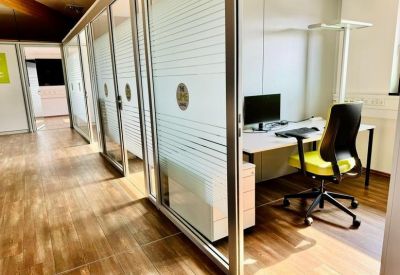 Glass-walled office corridor showing individual workstations and wooden floors.