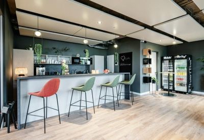 Modern breakroom kitchen with a long bar, colorful stools, and wood flooring.