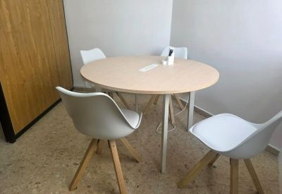 Small meeting area with a round light-wood table and four white chairs.