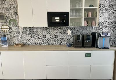 Kitchenette with patterned tile backsplash, white cabinetry, and coffee machines.