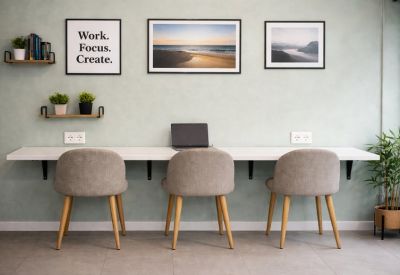 Long white desk with a laptop and two power outlets against a sage green wall.