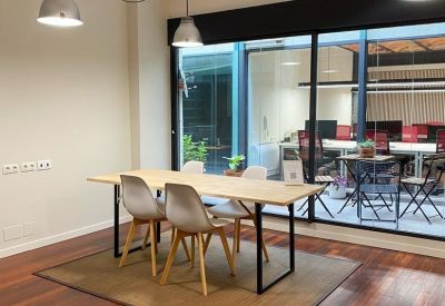 Breakout space with a wooden communal table, designer chairs, and large windows overlooking a courtyard.