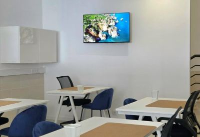 Modern coworking area with white desks, blue chairs, and a wall-mounted TV display.
