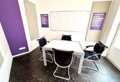 Meeting room with a central white table, four black chairs, and a whiteboard.