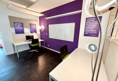 Bright office corner with a purple accent wall, white whiteboard, and a green-trimmed ergonomic chair.