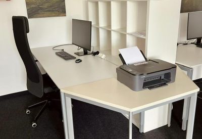Desk area with a computer, printer, and white shelving unit against a wall with mountain art.
