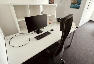Single workstation with a white desk, monitor, and tall ergonomic chair.