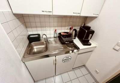 Compact office kitchenette featuring a sink, coffee machine, and white cabinetry.