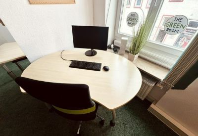 Sunlit curved corner desk with a view through a window featuring The Green Room logo.