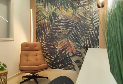 Modern lounge area with a tan leather armchair and tropical leaf pattern feature wall.