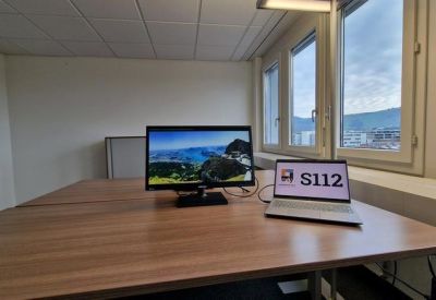 Office desk with laptop and monitor, adjacent to windows.