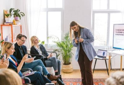Bright meeting room with people attending a presentation in a sunlit space with large windows.
