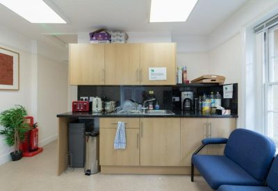 Communal kitchen area with light wood cabinetry, blue seating, and a coffee machine.