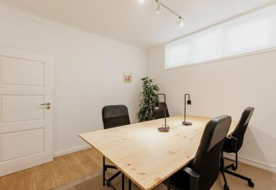 Minimalist meeting room with a wooden table, black chairs, and a potted plant.