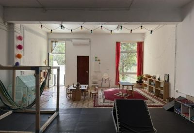 Bright communal lounge and play area with string lights, red rugs, and large windows.