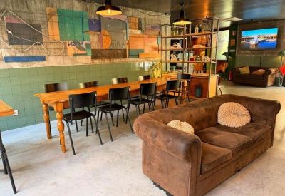 Lounge area featuring a long wooden communal table, brown leather sofa, and colorful wall art.