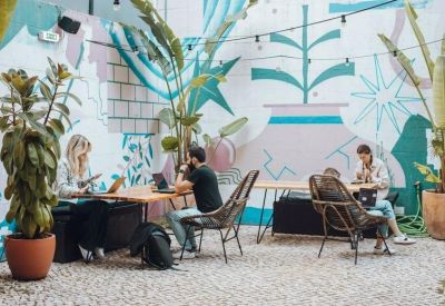 Outdoor collaborative workspace with people sitting at tables against a graphic mural and tropical plants.