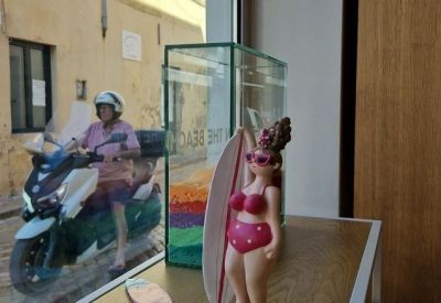 Close-up of a whimsical beach-themed figurine displayed in a glass case near a window.