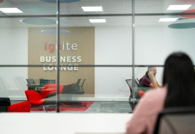 View through a glass wall into a lounge with bright red armchairs and branded wall.